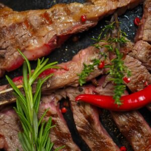 Close-up of a grilled beef steak garnished with red chili and fresh herbs, perfect for a savory meal.