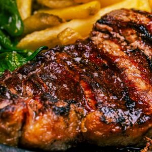 Close-up of a juicy grilled steak with sides of green peppers and fries. Perfect for a mouthwatering meal.