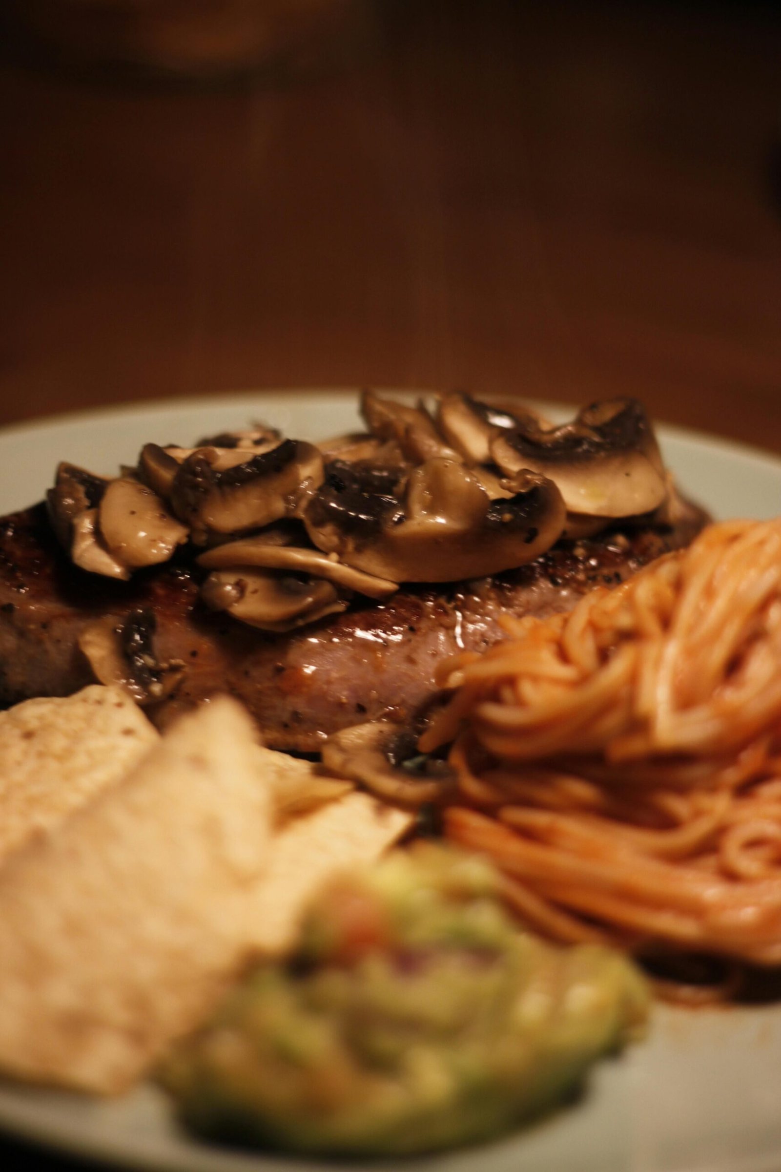 A delicious steak topped with mushrooms, served with pasta and guacamole.